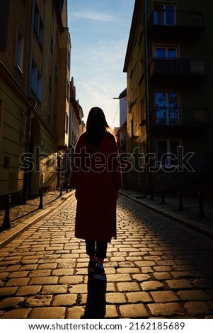 Rear view of tourist woman walking at european city street at sunset, Summer vacation