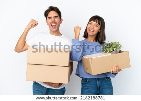 Young couple making a move while picking up a box full of things isolated on white background celebrating a victory