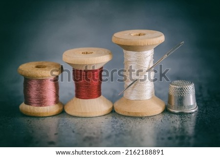 Multi-colored threads on a wooden spool and a sewing needle on an old surface. Multicolor background of sewing threads. retro style 