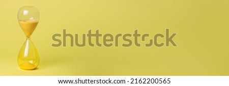 Yellow hourglass on yellow background banner. Passing time or deadline concept. Royalty-Free Stock Photo #2162200565