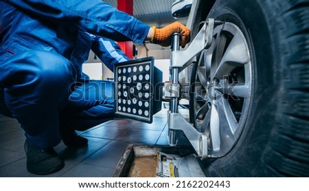 Auto mechanic installing sensor during suspension adjustment and automobile wheel alignment work at repair service station. Close up Royalty-Free Stock Photo #2162202443