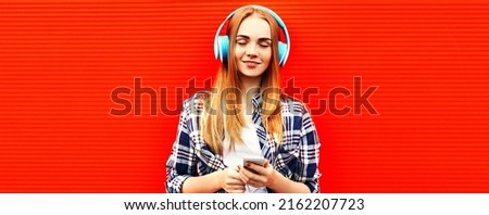 Portrait of happy woman with smartphone in wireless headphones listening to music on red background, blank copy space for advertising text