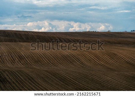 Rows of soil before planting. Drawing of furrows on a plowed field prepared for spring sowing of agricultural crops. View of the land prepared for planting and growing crops. Royalty-Free Stock Photo #2162215671