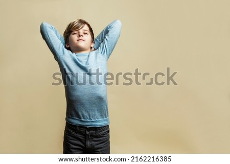 A 9-year-old boy stretches tiredly. A handsome guy in a blue sweater and gray jeans. Difficulties in leaning and stress. Yellow background. Space for text.