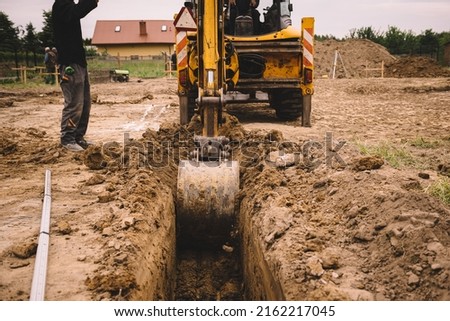 Excavator working at house construction site - digging foundations for modern house. Beginning of house building. Earth moving and foundation preparation. Royalty-Free Stock Photo #2162217045
