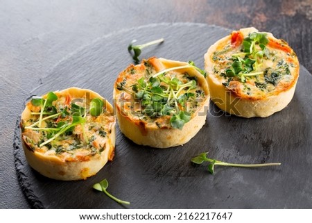 Savoury mini quiches with custard and watercress on a black round wooden board Royalty-Free Stock Photo #2162217647