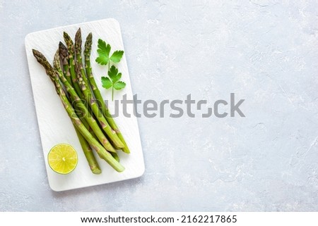 asparagus stems on the rectangular plate served with green lemon and parsley, grey concrete background, top view, copyspace