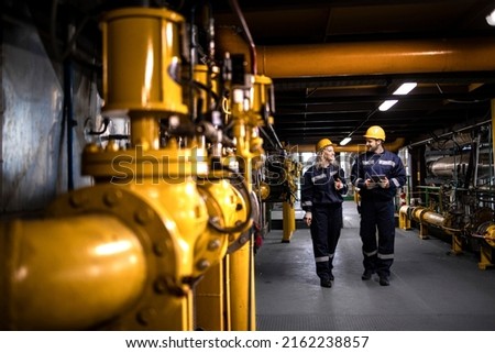 Oil and gas refinery production. Factory workers in safety equipment walking by gas pipes and checking distribution and consumption. Royalty-Free Stock Photo #2162238857