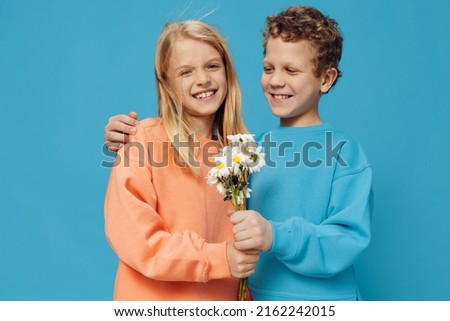 joyful, cute children stand on a blue background holding a bouquet of daisies in their hands and looking at it.