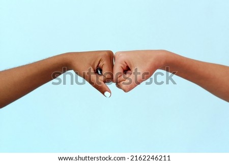 Black African American woman and white Caucasian woman punching on a blue background. Partnership and cooperation agreement, multiracial diversity and immigration concept. Stop racism. Royalty-Free Stock Photo #2162246211