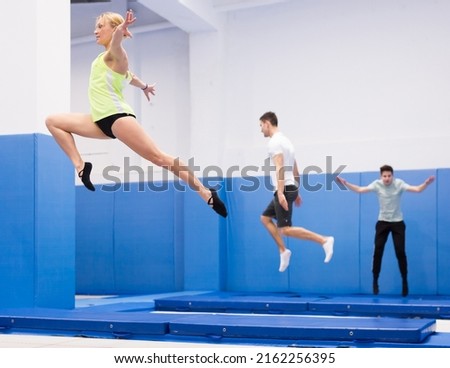 Focused female gymnast jumping on professional trampoline, practicing movements in jump during training..