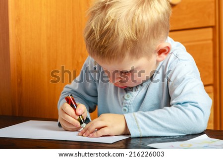 Happy childhood. Blonde boy child kid with pen writing drawing on paper doing homework. At home.