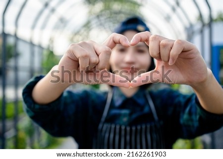 Close up of a smiling female farmer making hands shape heart sign at an organic farm, customer care, service mind, friendliness.