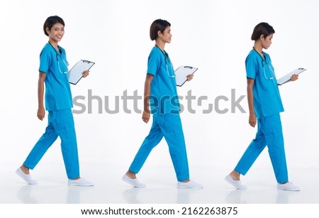 Full length 20s young Asian Nurse Woman wear stethoscope; blue uniform, walking forward right left. Hospital female carry patient chart data happy smile over white background isolated