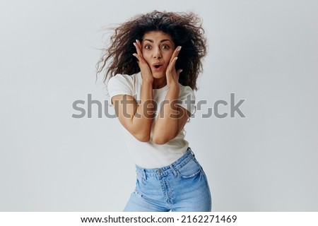 COOL SALE OFFER. Shocked curly Latin woman look at camera, touch cheek and say Wow. Copy space for fashion brands accessories and clothing, free place for ad. Studio shoot isolated white background