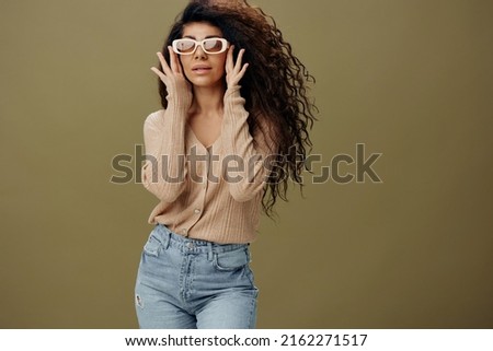 TRENDY EYEWEAR CONCEPT. Smiling pretty tanned curly Latin female in casual things wear sunglasses posing isolated over pastel olive green background. Copy space Mockup Banner. Fashion offer