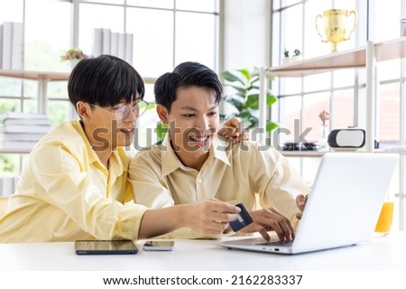 Portrait of carefree gay couple, lgbt man holding credit card enjoy shopping online together at home. Lgbt man, cute male gay couple spend time at home use laptop shopping on line.