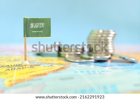 Selective focus of Saudi Arabia flag in blurry world map with coins. Saudi economy and wealth concept.