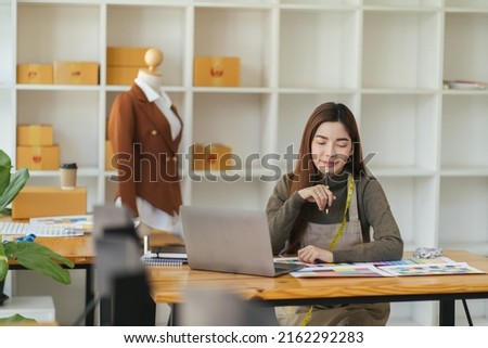 Asian woman designer are thinking and drawing something on paper for customers order items at the designer desk in the studio. Clothes designers are working in the office. Startup designer concept.