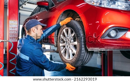Expert specialist technician changes tires, tyres of lifted up car at auto service, wears uniform costume. Royalty-Free Stock Photo #2162293019