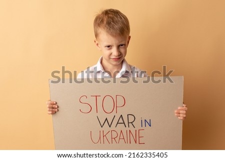 Portrait of a little boy calls to stop the war in Ukraine, raises a banner with the inscription Stop the war in Ukraine, hides behind a poster. No war, stop war.