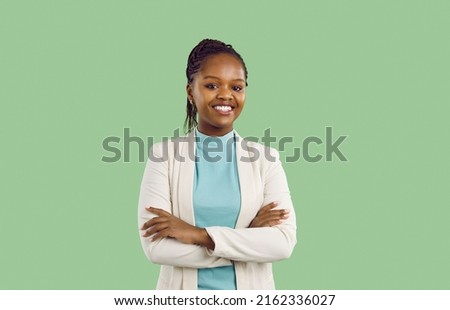 Studio portrait of black businesswoman with toothy smile. Confident good looking young woman with Afro braids, in white jacket and mint turtleneck standing isolated on solid green colour background Royalty-Free Stock Photo #2162336027