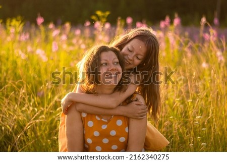 Portrait of a smiling happy Caucasian mother with her daughter in orange dresses on the background of a sunset field, An adult daughter kisses her mother. The concept of the Mother's Day holiday