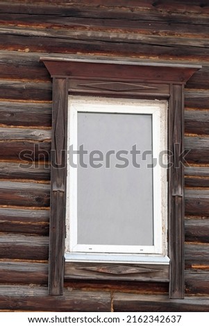 White plastic window with wooden platbands on a log cabin. Meto for photo caption