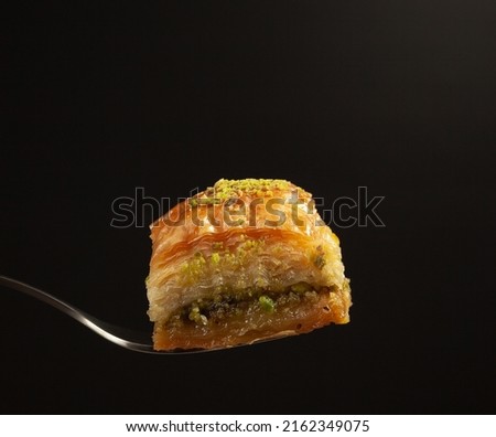 one delicious honey baklava with pistachios on a fork on a black background, side view Royalty-Free Stock Photo #2162349075