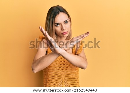 Young caucasian blonde woman wearing casual yellow t shirt rejection expression crossing arms doing negative sign, angry face 