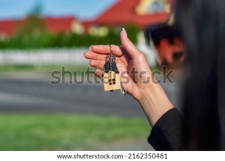 A woman holds in her hands the keys to the house against the background of residential buildings. Concept for buying and renting apartments