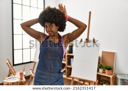 Young african american woman with afro hair at art studio doing bunny ears gesture with hands palms looking cynical and skeptical. easter rabbit concept. 
