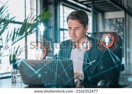 Handsome businessman in suit at workplace working with laptop to hire new employees for international business consulting. HR, social media hologram icons over office background