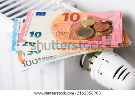 Euro money banknotes on heating radiator battery with thermostat temperature regulator. Concept of expensive heating costs and rising energy bill prices for winter cold season. Royalty-Free Stock Photo #2162356903