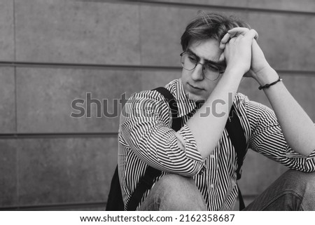 Portrait Depressed male student sitting on city street black and white photo