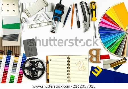 Аdvertising agency tools, accessories and material samples. Palette of film colours, film squeegee, aluminium profile and plastic samples and instruments on the white background. Top view. No people.