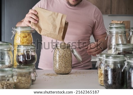 Unrecognizable latin man filling up a jar with oat flakes from a paper bag. Food in bulk delivery. Royalty-Free Stock Photo #2162365187