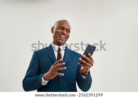 Cheerful african american businessman watching smartphone. Bald adult man wearing suit. Concept of modern successful male lifestyle. Isolated on white background. Studio shoot. Copy space Royalty-Free Stock Photo #2162391299