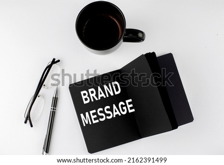 BRAND MESSAGE written text in small black notebook with coffee , pen and glasess on a white background. Black-white style