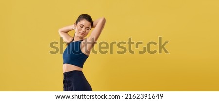 Slim female in sports bra keeping hands behind head and stretching body during exercises. Side view of girl with closed eyes, resting, isolated on orange studio background. Concept of relaxation.