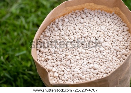 Close-up view of paper bag with fertilizer on green grass. Fertilizing concept Royalty-Free Stock Photo #2162394707