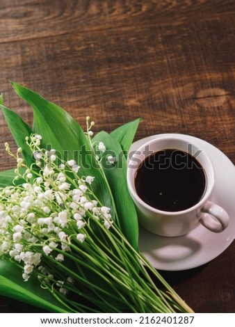 Good spring morning, a bouquet of blooming lilies of the valley and a cup of coffee on a wooden table