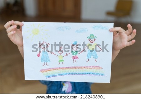 Close up little child showing her drawn of happy family. Family of mother, father and two children staying on rainbow. Happy concept of intimacy and togetherness.
