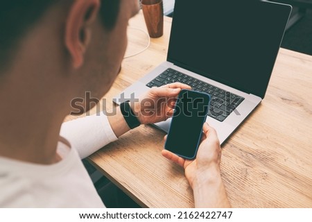 Man addicted to his phone surfing the social media on his phone while must works with his laptop