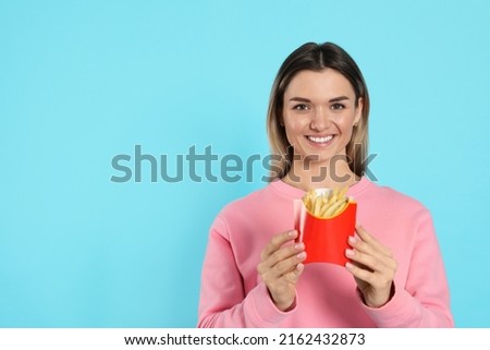 Young woman with French fries on light blue background, space for text
