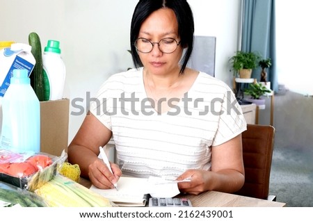 High cost inflation concept. Taking inventory of checking account, all credit cards and receipts from the supermarket.Woman headache stress from inflation crisis high cost gas electric energy bills. Royalty-Free Stock Photo #2162439001