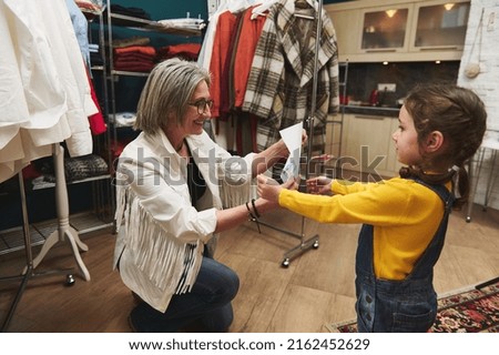 Loving caring granny smiles as she looks at her granddaughter's drawing while working in a tailoring and designing atelier. Family relationships