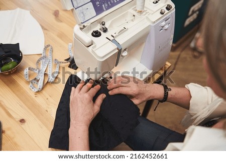 Overhead view of a female fashion designer dressmaker tailor seamstress sewing clothes on sewing machine in a tailoring atelier. Creating new garment, fashion designer business start-up concept Royalty-Free Stock Photo #2162452661