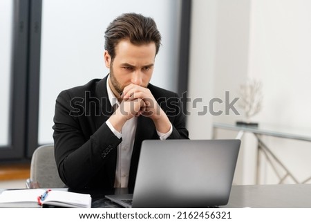 Puzzled young businessman in formal wear sitting at desk in office and watching at laptop screen with despair, frustrated male office employee in suit received fired or bankruptcy notification Royalty-Free Stock Photo #2162456321