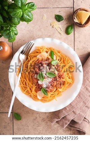 Pasta spaghetti Bolognese. Tasty appetizing italian spaghetti with bolognese sauce, tomato sauce, cheese parmesan and basil on white plate on old beige tiles table background. Top view.